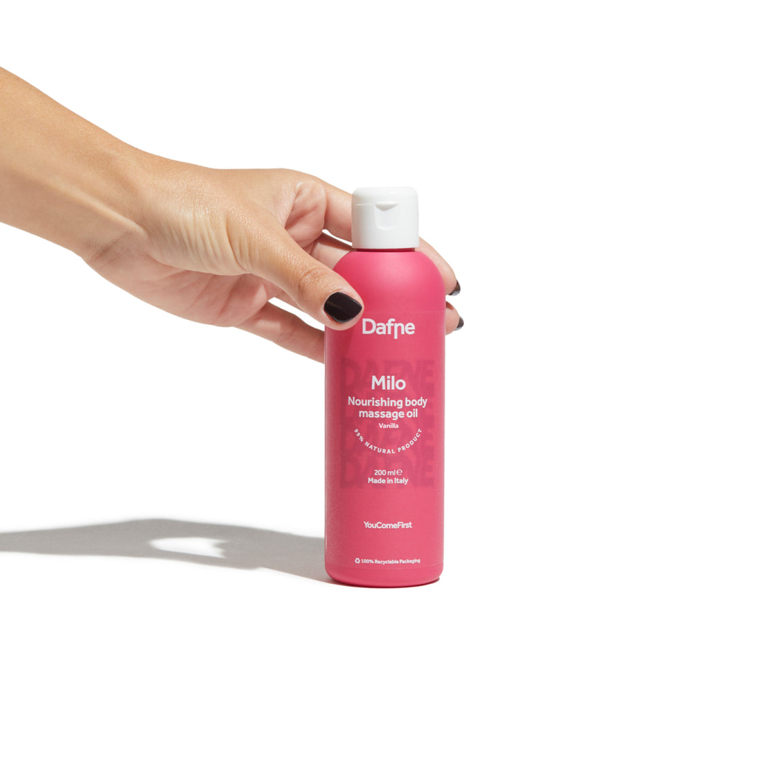 Olio massaggi Milo Dafne, alla vaniglia, naturale, in flacone magenta impugnato da una mano, su sfondo bianco